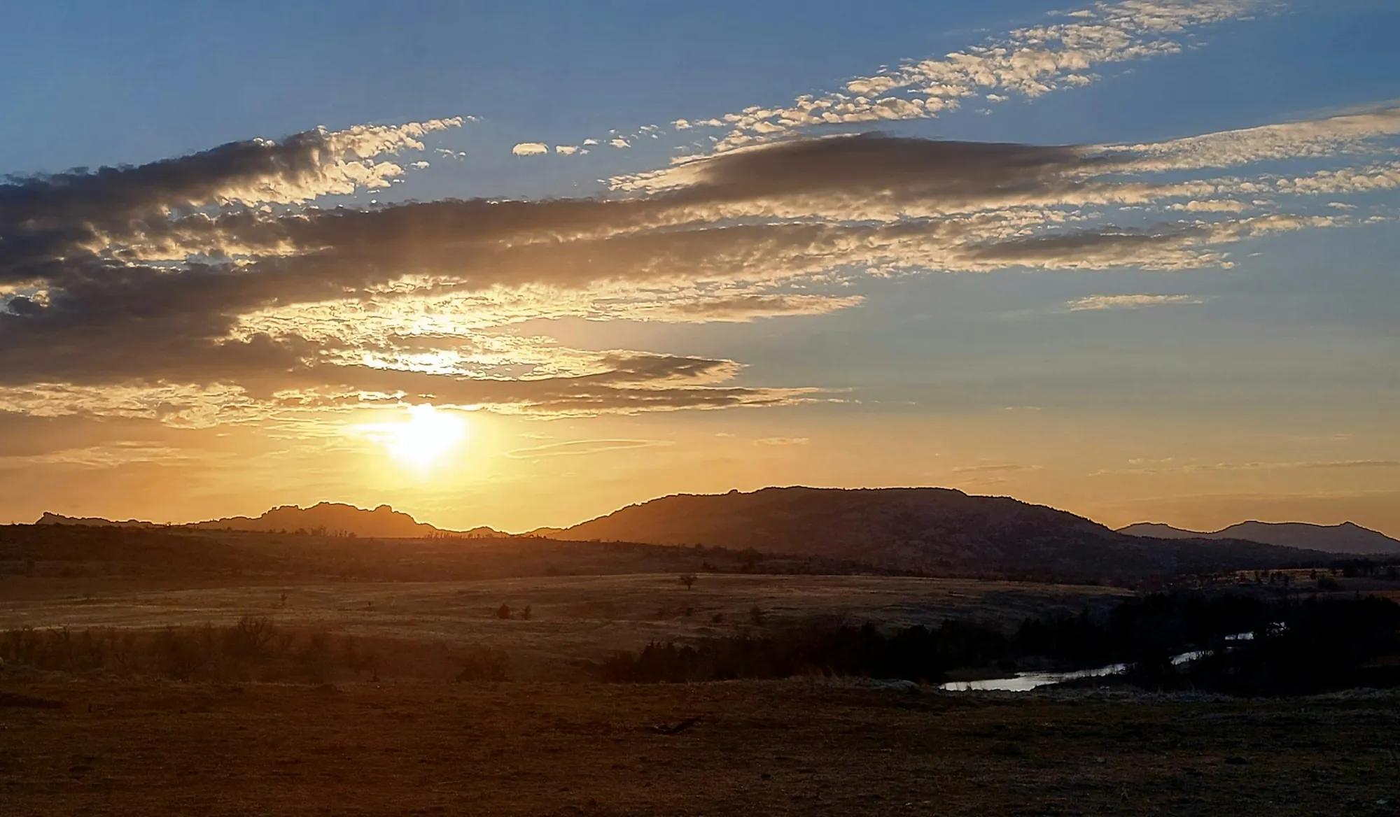 Golden-hour sunset over the Oklahoma prairie and distant mountains